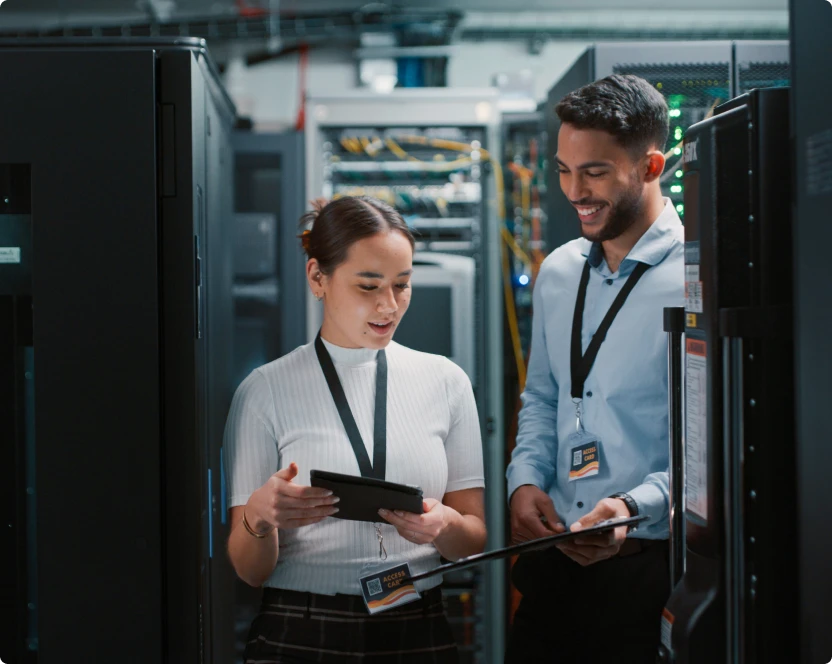 Ein Mann und eine Frau stehen in einem Serverraum und schauen auf ein Tablet