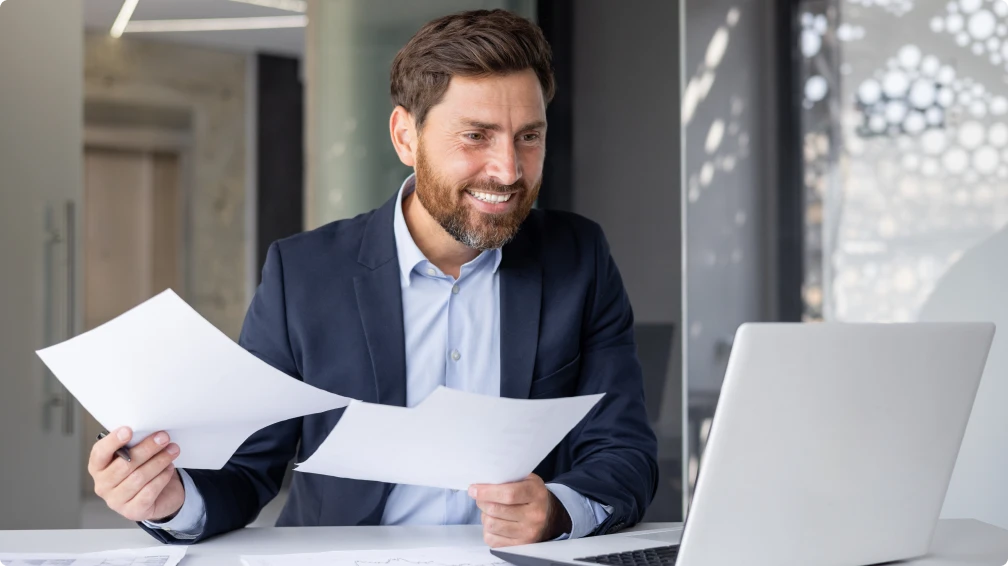Ein Mann sitzt an einem Schreibtisch und hält Papiere in der Hand