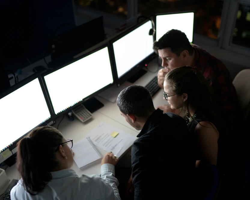 Eine Gruppe von Menschen sitzt an einem Schreibtisch und schaut auf Computerbildschirme