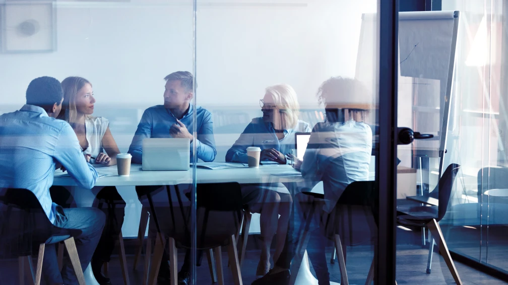 Eine Gruppe von Menschen sitzt um einen Tisch mit Laptops
