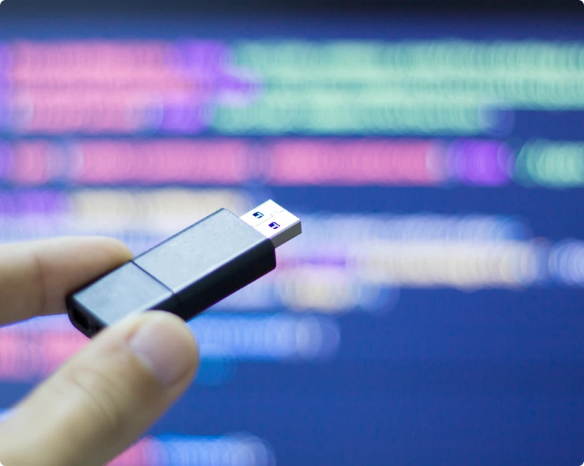 Eine Person hält einen USB-Stick in der Hand vor einem Computerbildschirm