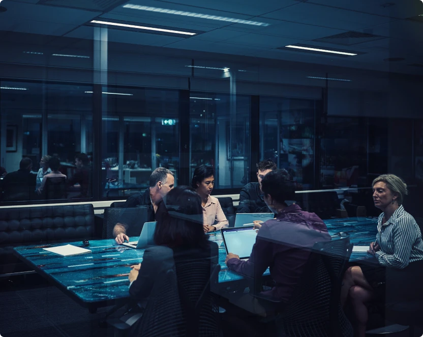 Eine Gruppe von Menschen sitzt um einen Tisch und arbeitet an Laptops