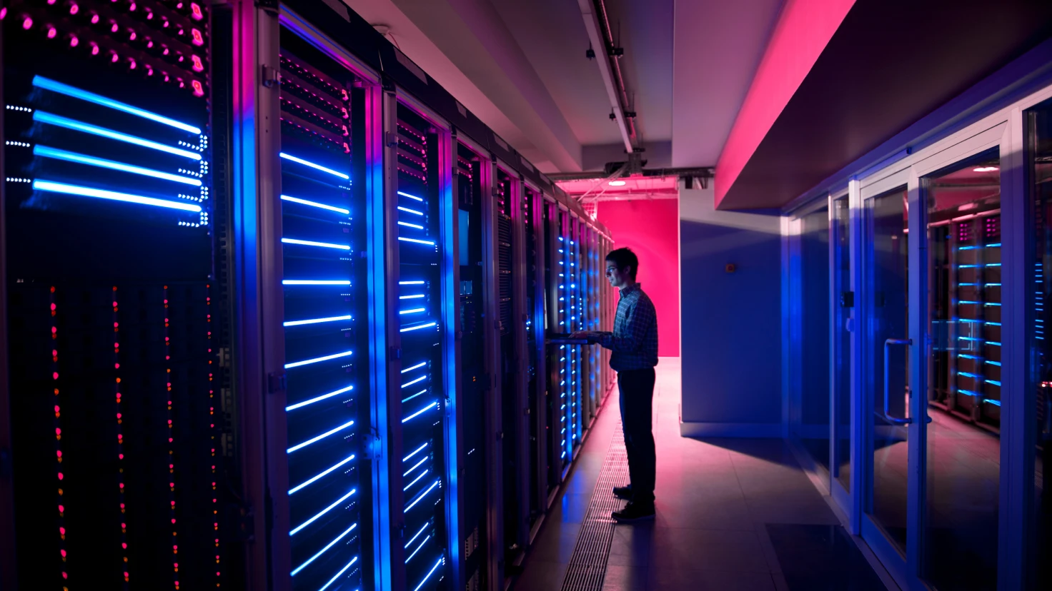 Ein Mann steht in einem Serverraum und arbeitet an einem Tablet