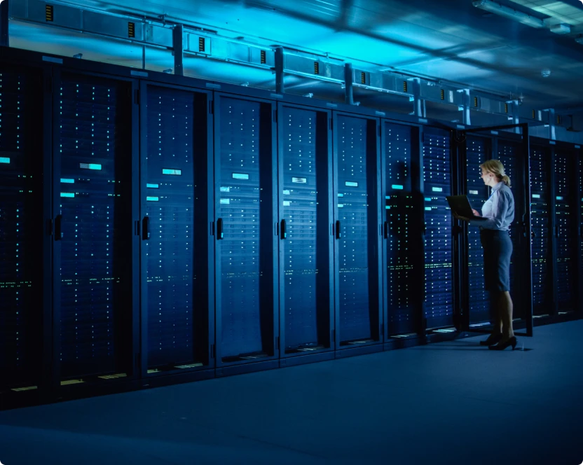 Eine Frau steht in einem Serverraum und benutzt einen Laptop