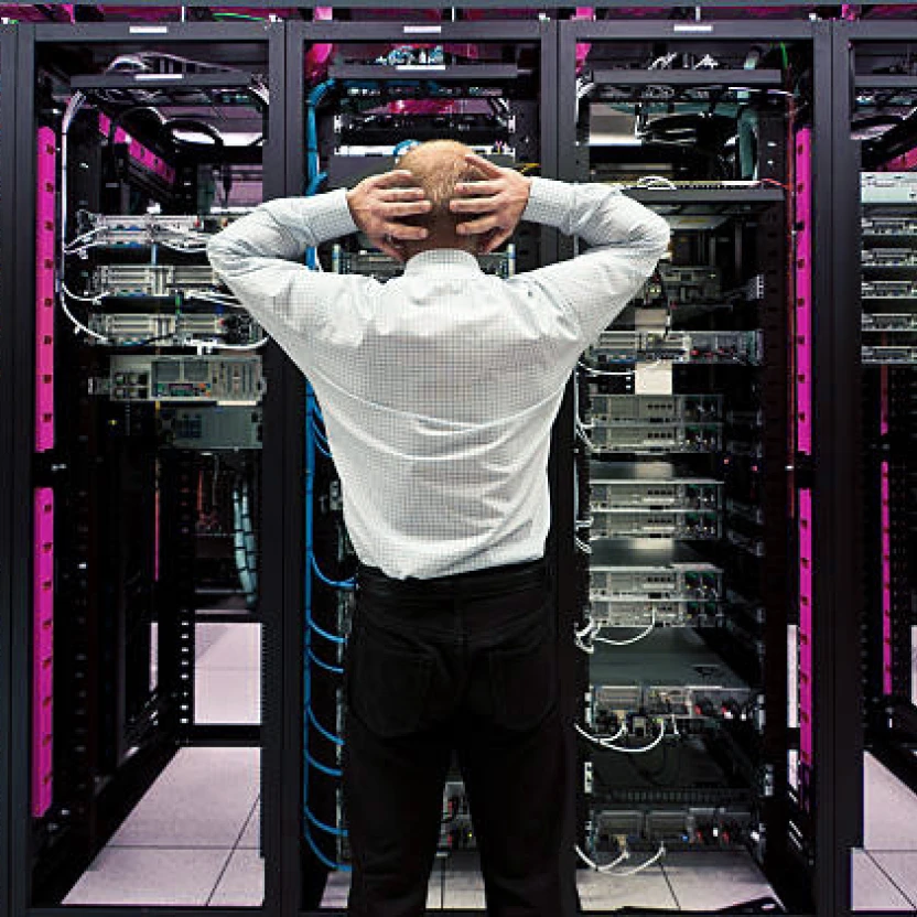 Ein Mann steht in einem Serverraum und hält seine Hände hinter dem Kopf