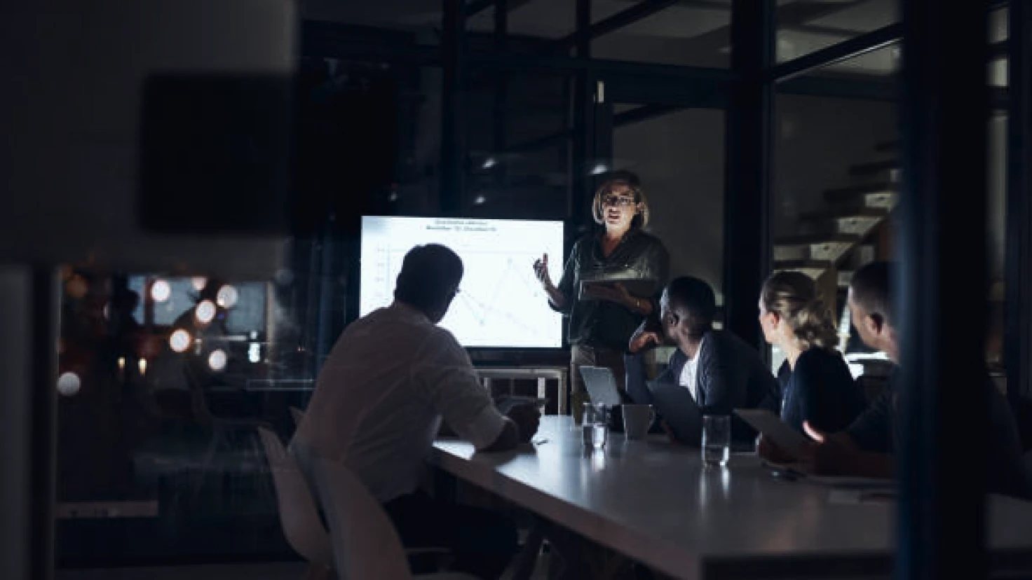 Eine Gruppe von Menschen sitzt um einen Tisch und hört einer Frau zu